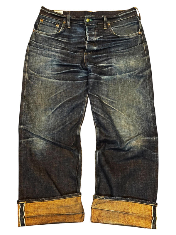 A pair of dark blue denim jeans with a faded wash and rolled cuffs showing a tan lining, photographed flat against a white background.