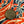 A round bronze-colored metal button featuring crossed shovel and pickaxe symbols and the year '1998', shown on a patterned fabric background with red, navy, and cream stripes.