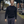 Man wearing a dark sweater and gray pants standing on a street with cars and trees in the background.